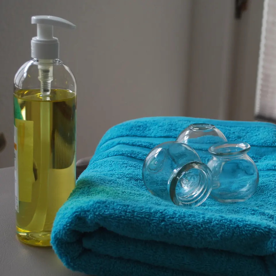 Flacon d’huile de massage et ventouses en verre posées sur une serviette turquoise, au cabinet